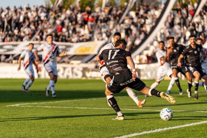 A dynamic football match with players in motion on a sunny day, witnessed by a packed stadium.